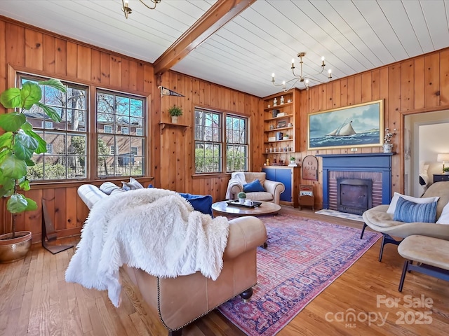 living area featuring wooden walls, beam ceiling, a fireplace, an inviting chandelier, and hardwood / wood-style flooring