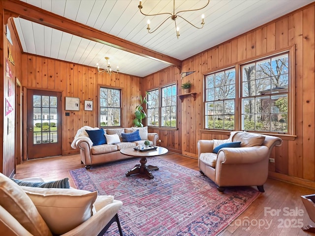 living room with a wealth of natural light, beam ceiling, a notable chandelier, and hardwood / wood-style flooring