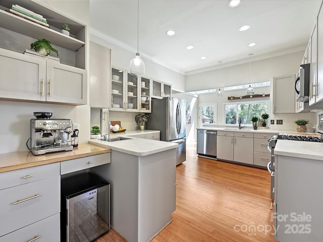 kitchen with light wood-style flooring, decorative light fixtures, appliances with stainless steel finishes, and ornamental molding