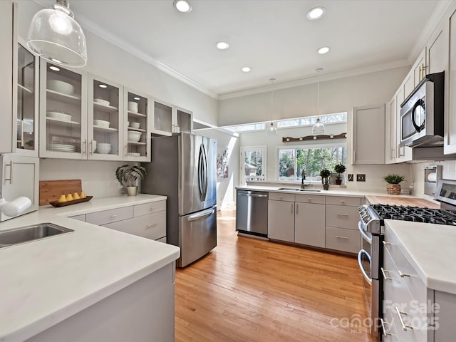 kitchen with light wood-style flooring, appliances with stainless steel finishes, pendant lighting, and ornamental molding