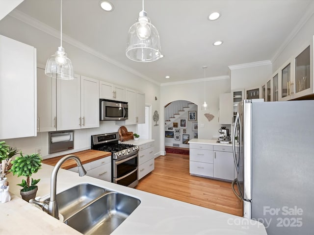 kitchen with light wood finished floors, ornamental molding, a sink, white cabinets, and appliances with stainless steel finishes