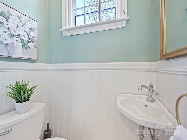 bathroom featuring a wainscoted wall, toilet, and a sink