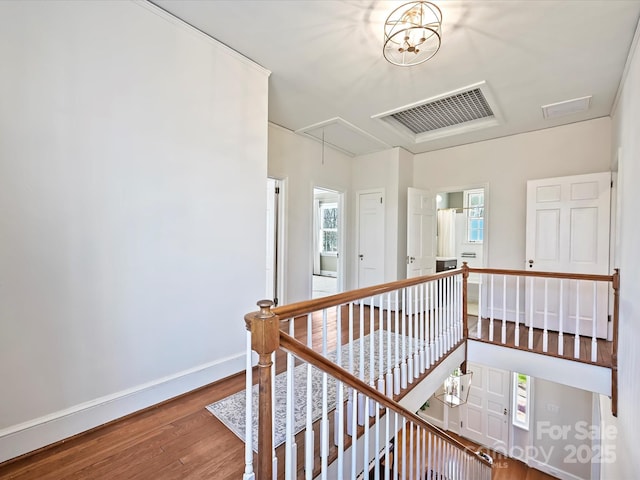 hallway with wood finished floors, baseboards, visible vents, attic access, and an upstairs landing