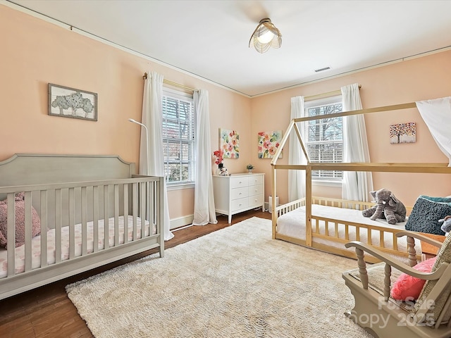 bedroom featuring a crib, wood finished floors, and visible vents