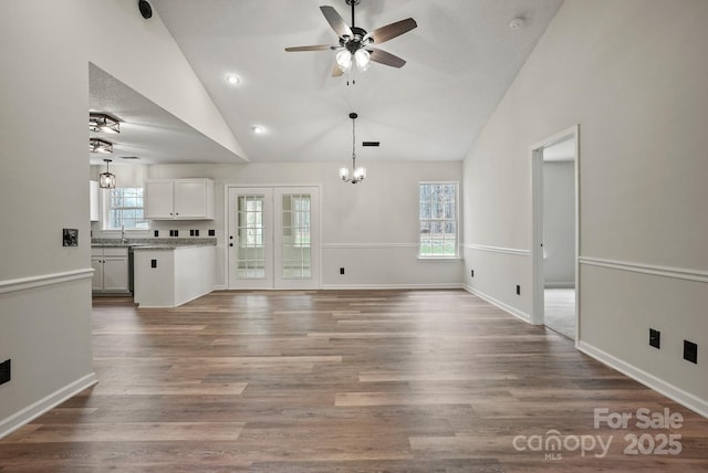 unfurnished living room featuring a sink, ceiling fan with notable chandelier, high vaulted ceiling, and wood finished floors