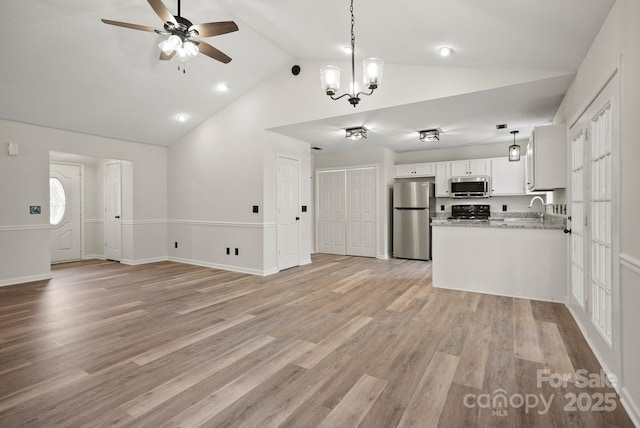 unfurnished living room with a ceiling fan, a sink, light wood-style floors, baseboards, and vaulted ceiling