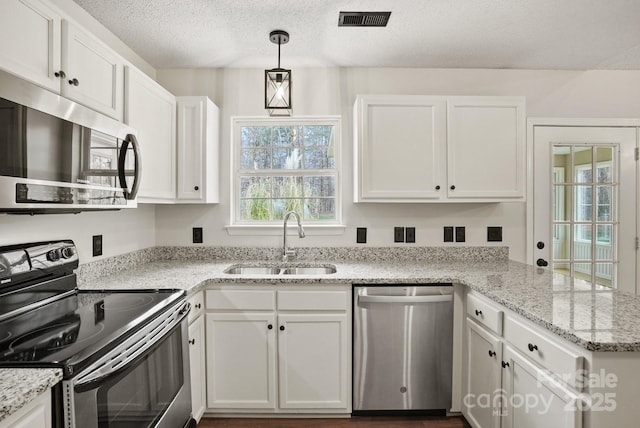 kitchen featuring visible vents, a sink, a peninsula, appliances with stainless steel finishes, and white cabinets