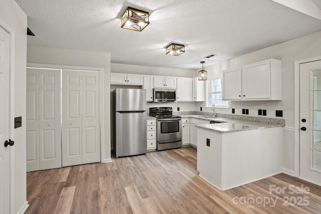 kitchen featuring light wood finished floors, appliances with stainless steel finishes, white cabinetry, and a peninsula