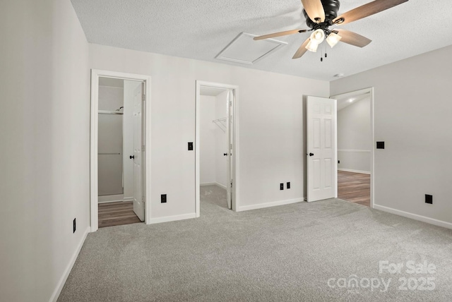 unfurnished bedroom featuring carpet, baseboards, attic access, a spacious closet, and a textured ceiling