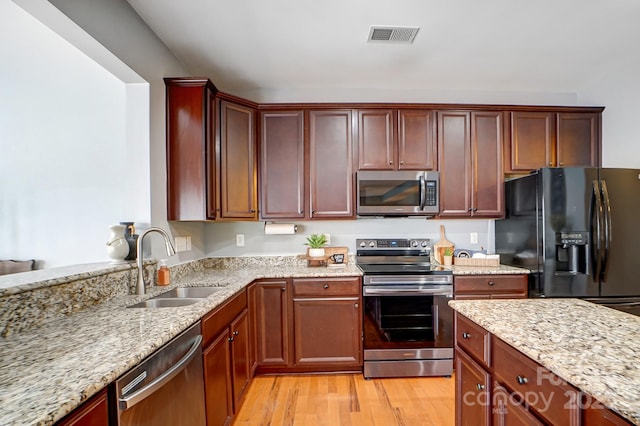 kitchen with visible vents, light wood-style flooring, stainless steel appliances, a sink, and light stone counters