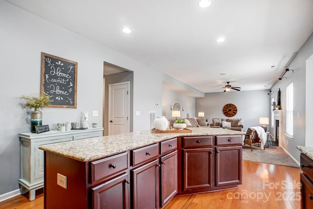 kitchen with open floor plan, light wood-type flooring, a kitchen island, reddish brown cabinets, and ceiling fan