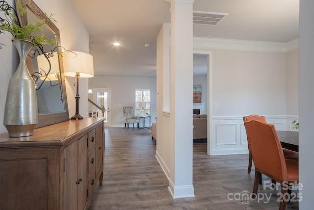 hallway with dark wood-style floors, a wainscoted wall, ornate columns, and ornamental molding