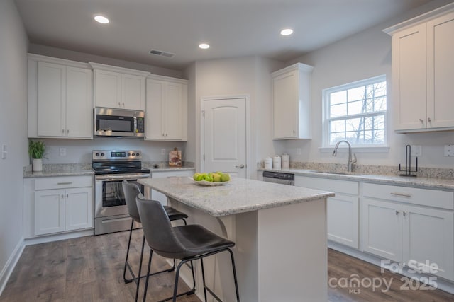 kitchen featuring visible vents, a kitchen island, a sink, appliances with stainless steel finishes, and white cabinetry