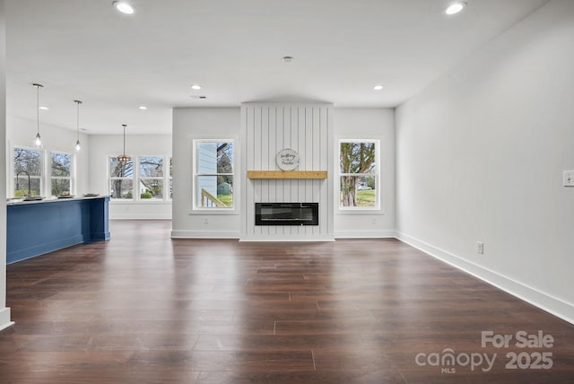 unfurnished living room featuring a fireplace, recessed lighting, dark wood-style floors, and a healthy amount of sunlight