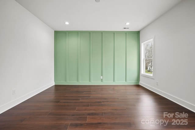 empty room with visible vents, recessed lighting, a decorative wall, and dark wood-style flooring