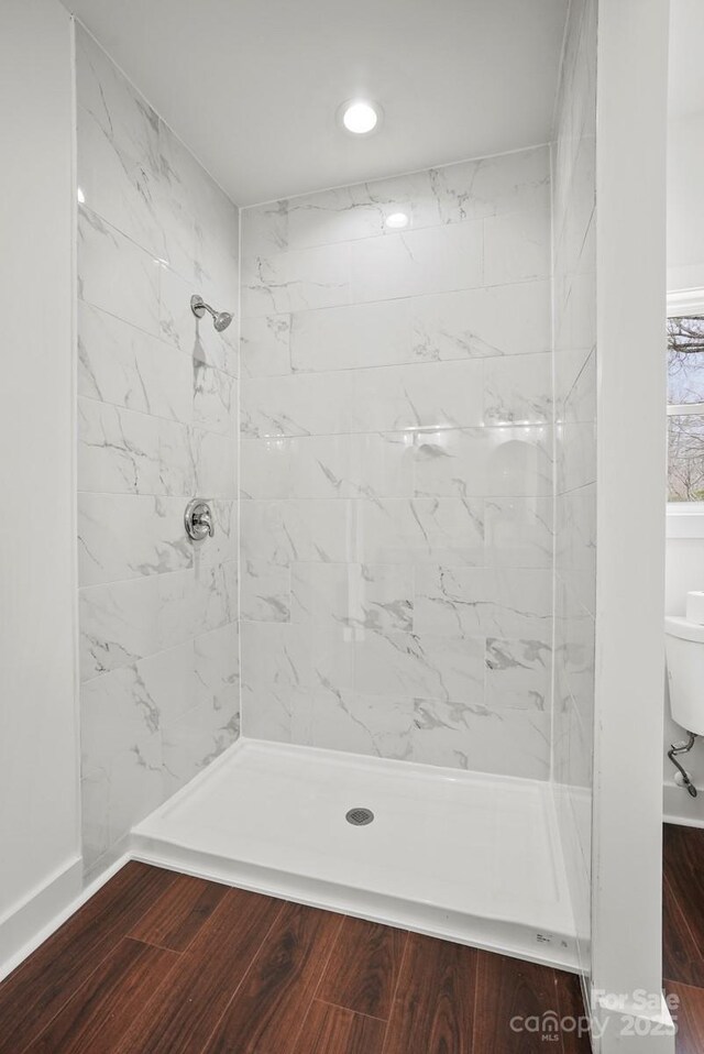 bathroom with toilet, tiled shower, and wood finished floors