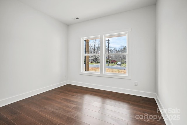 empty room featuring visible vents, baseboards, and dark wood finished floors