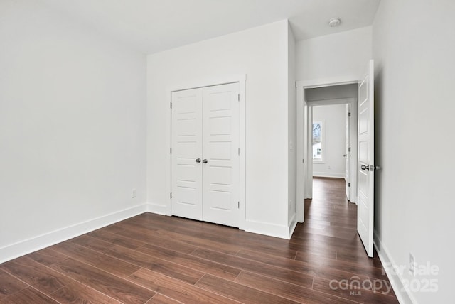 unfurnished bedroom with baseboards, dark wood-style flooring, and a closet