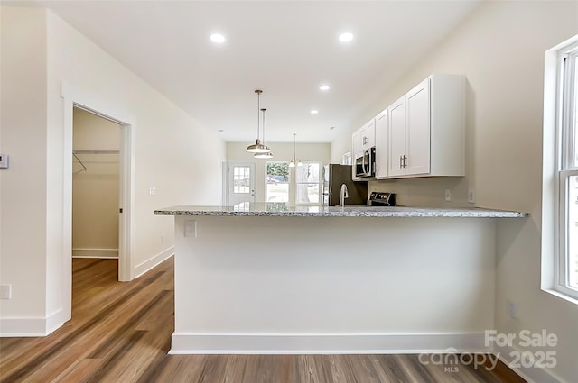 kitchen with decorative light fixtures, white cabinetry, appliances with stainless steel finishes, a peninsula, and light stone countertops