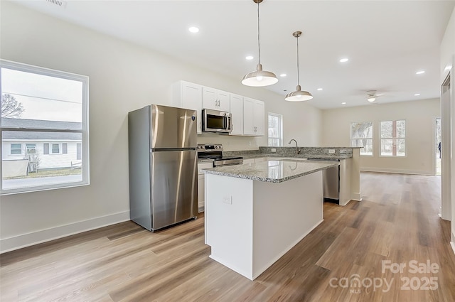 kitchen featuring a sink, a center island, stainless steel appliances, a peninsula, and light wood finished floors