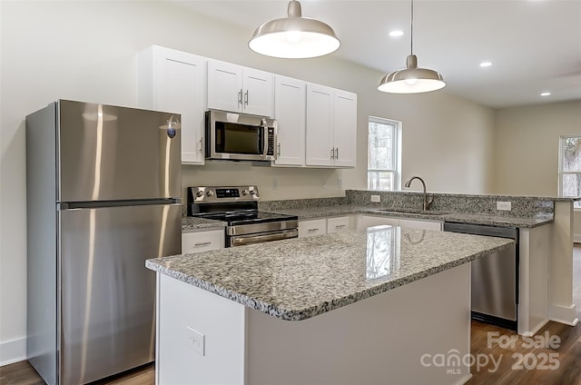 kitchen featuring light stone counters, a peninsula, a sink, stainless steel appliances, and white cabinets