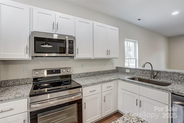 kitchen with a sink, light stone counters, appliances with stainless steel finishes, and white cabinets