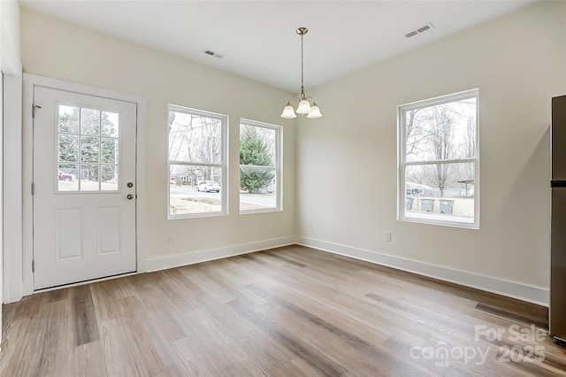 unfurnished dining area featuring baseboards, wood finished floors, visible vents, and a chandelier