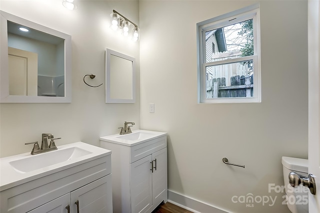 bathroom featuring toilet, two vanities, baseboards, and a sink