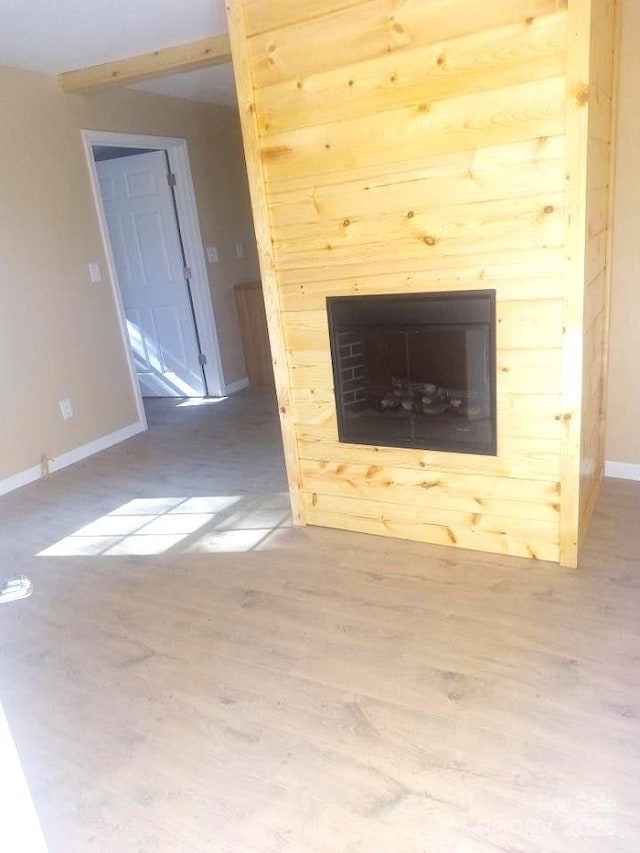 unfurnished living room featuring a glass covered fireplace, baseboards, and wood finished floors