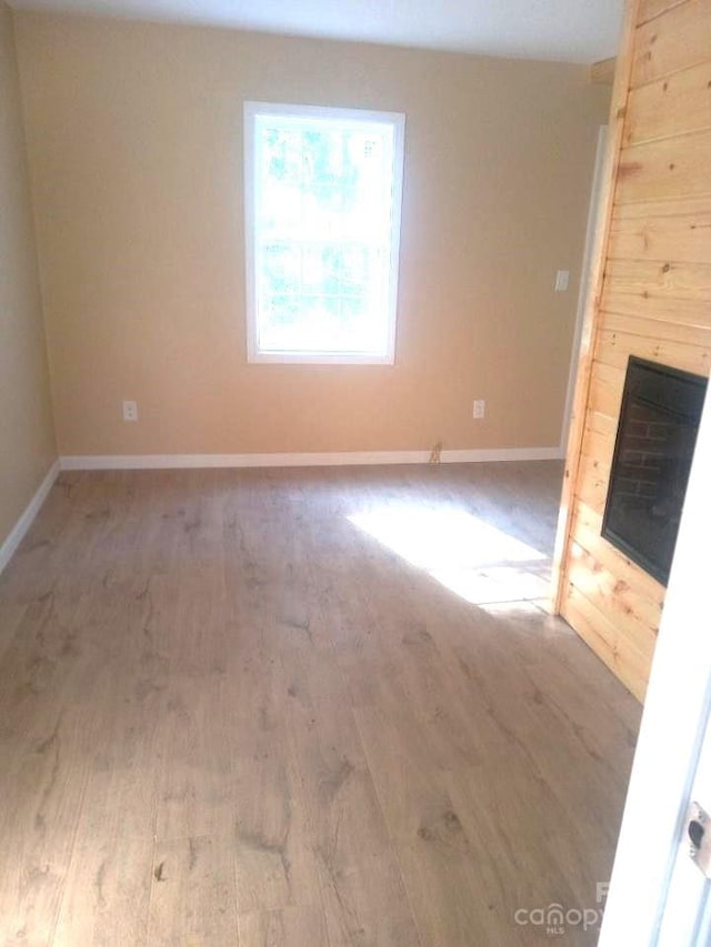 unfurnished room with wood finished floors, baseboards, and a large fireplace