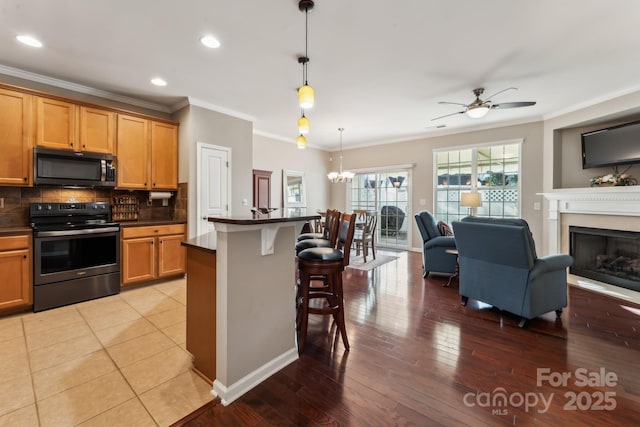 kitchen featuring a kitchen bar, ceiling fan with notable chandelier, tasteful backsplash, dark countertops, and stainless steel electric range