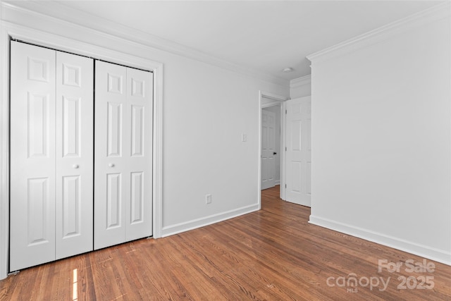 unfurnished bedroom with baseboards, ornamental molding, wood finished floors, and a closet