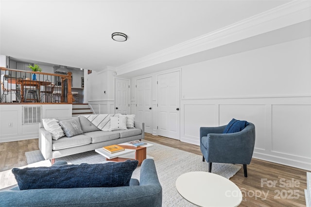 living area with stairs, ornamental molding, visible vents, and wood finished floors