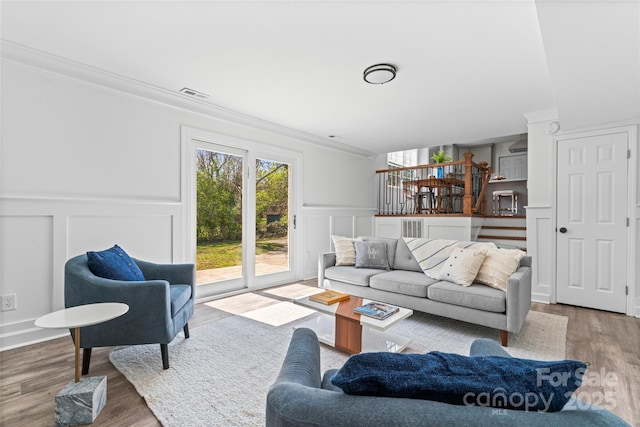 living room featuring a decorative wall, visible vents, crown molding, wood finished floors, and wainscoting