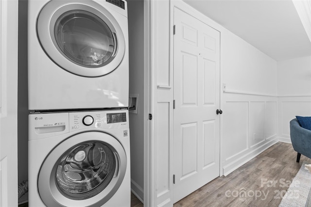 laundry area with a wainscoted wall, stacked washer and dryer, a decorative wall, laundry area, and wood finished floors