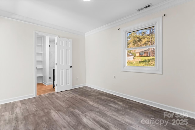 unfurnished bedroom with a walk in closet, ornamental molding, baseboards, visible vents, and wood finished floors