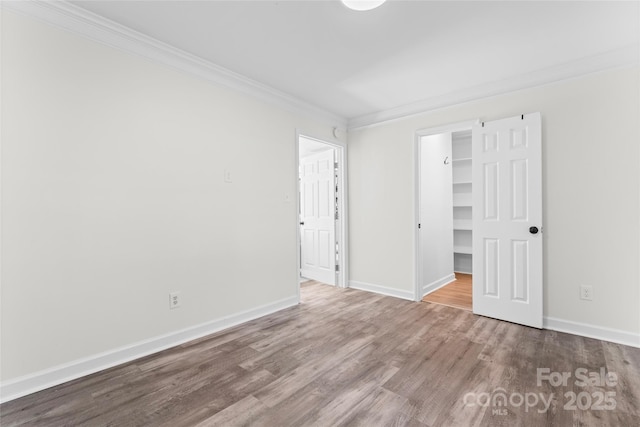 unfurnished bedroom with baseboards, ornamental molding, wood finished floors, and a walk in closet