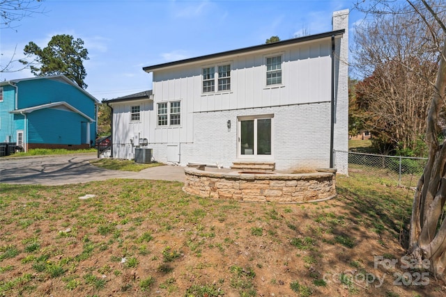 back of house featuring central air condition unit, a chimney, fence, and board and batten siding