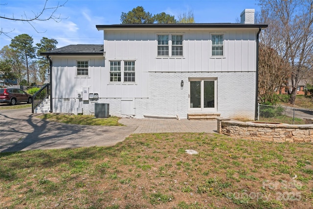 rear view of property with a chimney, fence, board and batten siding, a patio, and a lawn