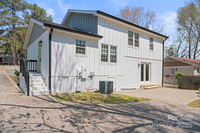 rear view of property featuring central air condition unit, a chimney, fence, and board and batten siding
