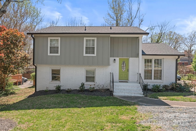 tri-level home featuring board and batten siding, a front yard, and brick siding