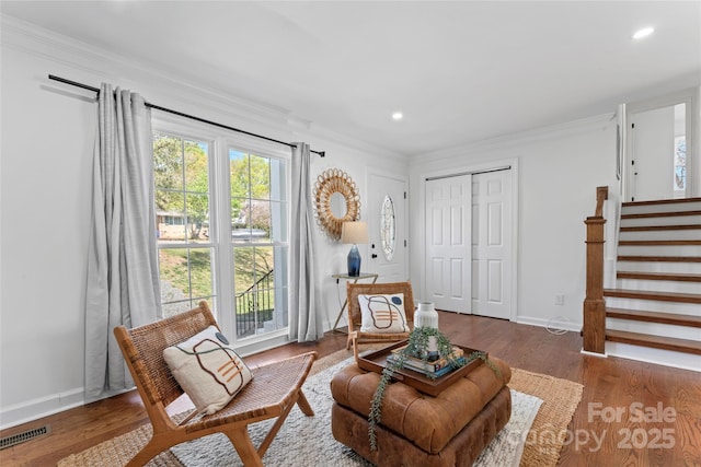 living area with wood finished floors, ornamental molding, baseboards, and visible vents