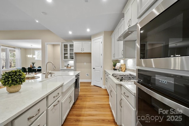 kitchen with under cabinet range hood, light wood-type flooring, stainless steel appliances, white cabinetry, and a sink