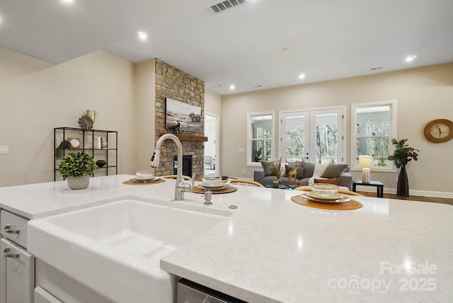 kitchen featuring visible vents, open floor plan, a stone fireplace, french doors, and a sink