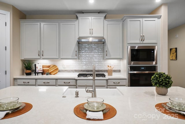 kitchen featuring under cabinet range hood, light countertops, tasteful backsplash, and appliances with stainless steel finishes