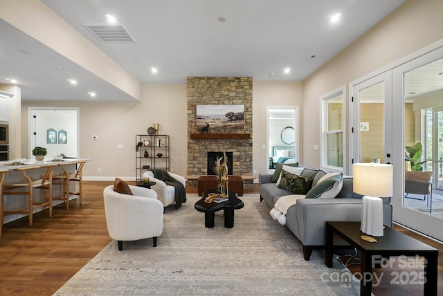 living area with visible vents, wood finished floors, recessed lighting, french doors, and a stone fireplace