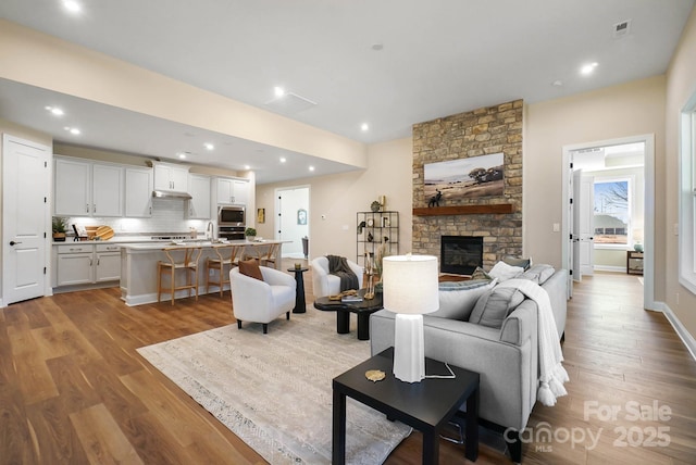 living area featuring visible vents, wood finished floors, recessed lighting, a stone fireplace, and baseboards