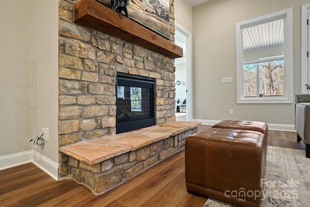 living room featuring baseboards, a stone fireplace, and dark wood-style floors