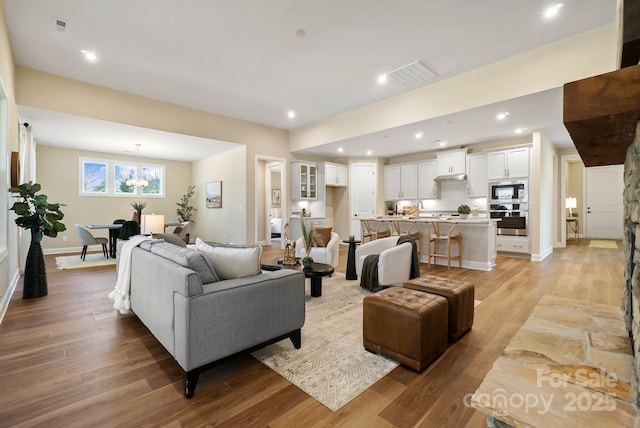 living room with visible vents, baseboards, light wood-style floors, and a chandelier