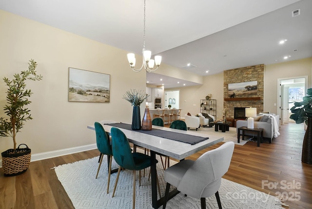 dining area with wood finished floors, visible vents, baseboards, a stone fireplace, and a chandelier